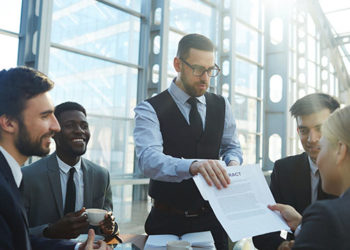 Portrait of modern businessman presenting contract documentation to group of people at table in bright sunlight