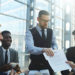 Portrait of modern businessman presenting contract documentation to group of people at table in bright sunlight